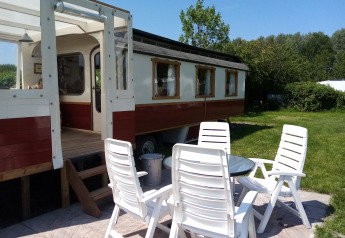 Udendørs siddeområde med hvide stole foran en traditionel rød og hvid vogn ved Klukkluk i Holland.
