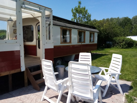 Zona de estar al aire libre con sillas blancas frente a una tradicional carreta roja y blanca en Klukkluk.