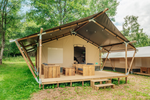 Tenda safari con veranda in legno e posti a sedere all'aperto immersa nel verde e circondata da alberi.