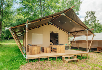 Tenda safari con veranda in legno e posti a sedere all'aperto immersa nel verde e circondata da alberi.