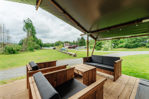 Covered outdoor seating area at a safari tent, featuring wooden furniture and a scenic grassy view.