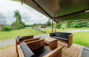 Covered outdoor seating area at a safari tent, featuring wooden furniture and a scenic grassy view.