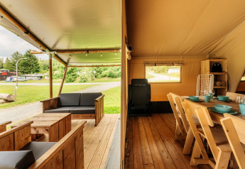 Inkijk in een safaritent met een houten terras en eethoek, omgeven door groene natuur.