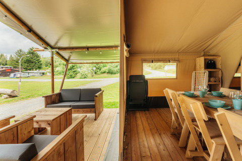 Vista dentro de una tienda safari con terraza de madera acogedora y comedor, rodeada de naturaleza verde.