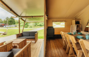 Vista dentro de una tienda safari con terraza de madera acogedora y comedor, rodeada de naturaleza verde.