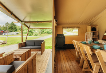 Inkijk in een safaritent met een houten terras en eethoek, omgeven door groene natuur.