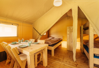 Vista interior de una tienda safari en Camping Braunlage, Alemania, con mesa, sillas y literas de madera.