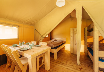 Interno di tenda safari al Camping Braunlage, Germania, con tavolo da pranzo, letto singolo e letti a castello.