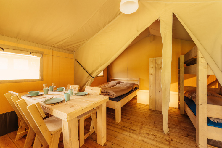 Vista interior de una tienda safari en Camping Braunlage, Alemania, con mesa, sillas y literas de madera.