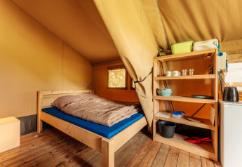 Interieur van een safaritent met houten bed, houten vloer en een open rek met servies en pannen.