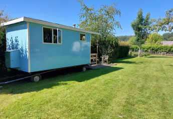 Casa rodante Pipowagen Snuitje azul en césped verde rodeada de árboles bajo un cielo despejado.