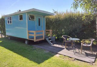 Casa rodante azul con terraza y muebles de jardín en Camping De Gouwe Stek, Países Bajos, con sol.