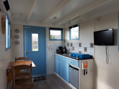 Cocina acogedora en Pipowagen Snuitje con armarios azules, TV y mesa en Camping De Gouwe Stek.