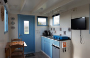 Cocina acogedora en Pipowagen Snuitje con armarios azules, TV y mesa en Camping De Gouwe Stek.