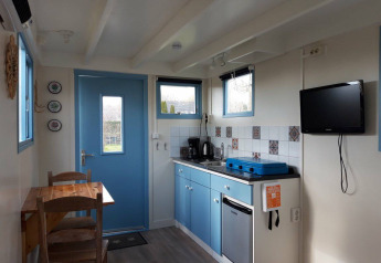 Cocina acogedora en Pipowagen Snuitje con armarios azules, TV y mesa en Camping De Gouwe Stek.