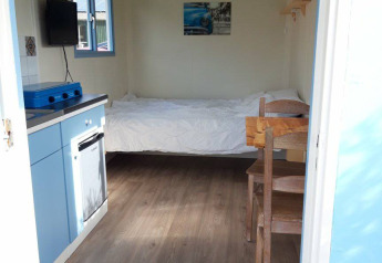 Vista interior de Pipowagen Snuitje en Camping De Gouwe Stek, cama, cocina pequeña y muebles de madera.