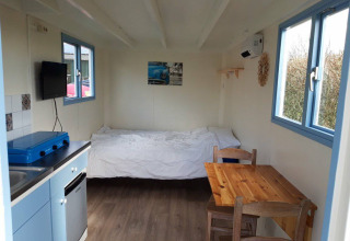 Interior de Pipowagen Snuitje en Camping De Gouwe Stek, Países Bajos, con cama, mesa y cocina.
