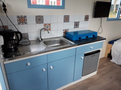 Pequeña cocina con gabinetes azules, estufa, cafetera y fregadero en Pipowagen Snuitje en Gouwe Stek.