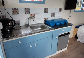 Pequeña cocina con gabinetes azules, estufa, cafetera y fregadero en Pipowagen Snuitje en Gouwe Stek.