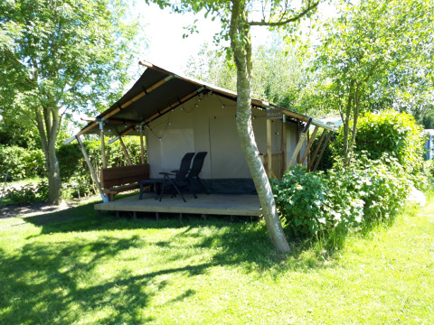 Safaritent Kievit lodge in een zonnige tuin met stoelen buiten en omringd door veel groen en bomen.
