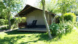 Safari-Zelt Kievit Lodge im Grünen mit Terrasse, Gartenmöbeln und umgeben von Bäumen und Sträuchern.