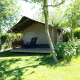 Lodge Safari tent Kievit en un área verde y soleada, con muebles de exterior y rodeada de vegetación.