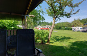 Vista desde la tienda Safari Kievit en Camping De Gouwe Stek, Países Bajos, con sillas y campo verde.