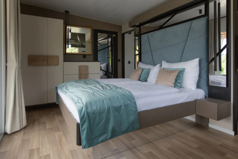 Alojamiento de glamping moderno en parque vacacional con cama flotante, ropa de cama elegante y luz natural.