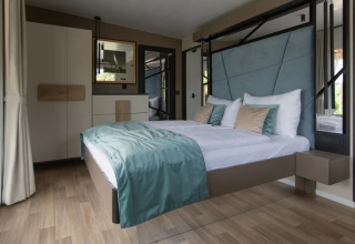 Alojamiento de glamping moderno en parque vacacional con cama flotante, ropa de cama elegante y luz natural.