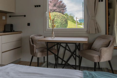 Moderne glamping accommodatie met twee zachte stoelen, een tafel en een raam met zicht op groene natuur.