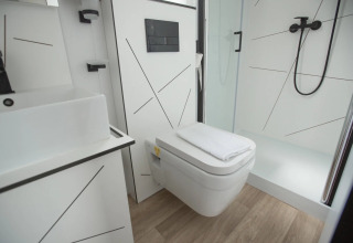 Bagno moderno con WC sospeso, doccia, lavandino e pavimento in legno chiaro in alloggio glamping.