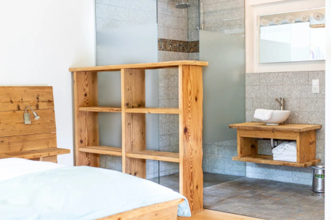 Lichte glampingkamer in vakantiepark met houten meubels, open douche en wastafel op houten blad.