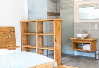 Lichte glampingkamer in vakantiepark met houten meubels, open douche en wastafel op houten blad.