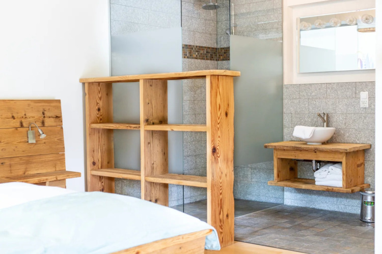 Bright glamping room at a holiday park featuring wood furniture, open shower, and a basin on a wood counter.