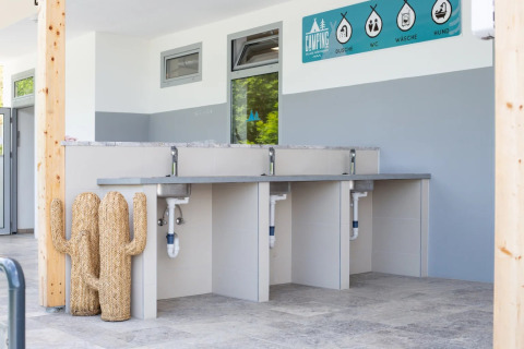 Moderne wasruimte op een glampingpark met drie wastafels, blauwe borden en een decoratieve rieten cactus.