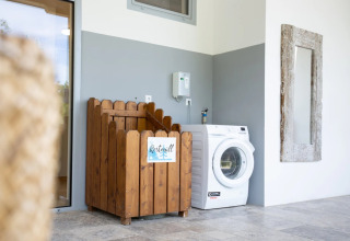 Area lavanderia moderna in un campeggio glamping con contenitore in legno, lavatrice e specchio a muro.