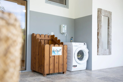 Area lavanderia moderna in un campeggio glamping con contenitore in legno, lavatrice e specchio a muro.