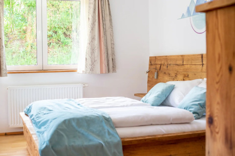 Helles Glamping-Schlafzimmer im Ferienpark mit Holzbett, großem Fenster und moderner Dekoration.