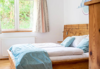 Camera glamping luminosa in un villaggio vacanze con letto in legno, grandi finestre e arredo moderno.