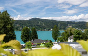 Uitzicht op een meer en heuvels vanuit een vakantiepark met glamping tenten en caravans onder blauwe hemel.