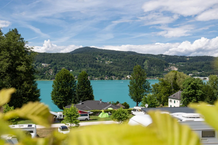 View of a lake and mountains from a holiday park with glamping tents and caravans under a blue sky.