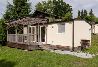 Glampingverblijf met houten terras en veranda in een groene vakantiewijk omgeven door bomen.