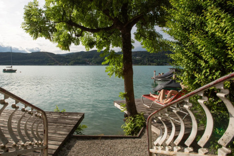 Vista desde unas escaleras hacia un lago con un árbol, muelles y persona descansando en resort glamping.