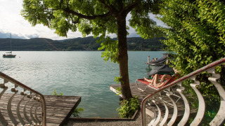 Vista desde unas escaleras hacia un lago con un árbol, muelles y persona descansando en resort glamping.