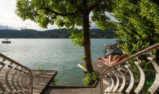View from steps leading to a lake with a tree, docks, and a person relaxing on a lounger at a holiday park.