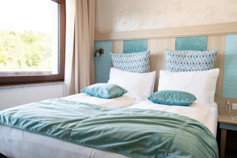 Letto accogliente con cuscini e coperta azzurri vicino alla finestra, sistemazione glamping in un parco vacanze.