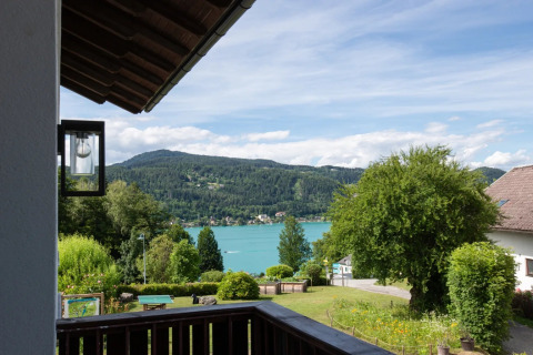 Blick von einem Ferienpark mit Glamping auf Garten, See und bewaldete Berge bei blauem Himmel.