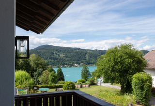 Vue depuis un parc de vacances avec glamping, sur un jardin, un lac et des montagnes boisées.