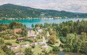 Feriepark med glampinghytter ved en sø, omgivet af skov, bjerge og naturskønne landskaber i baggrunden.