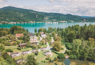 Feriepark med glampinghytter ved en sø, omgivet af skov, bjerge og naturskønne landskaber i baggrunden.
